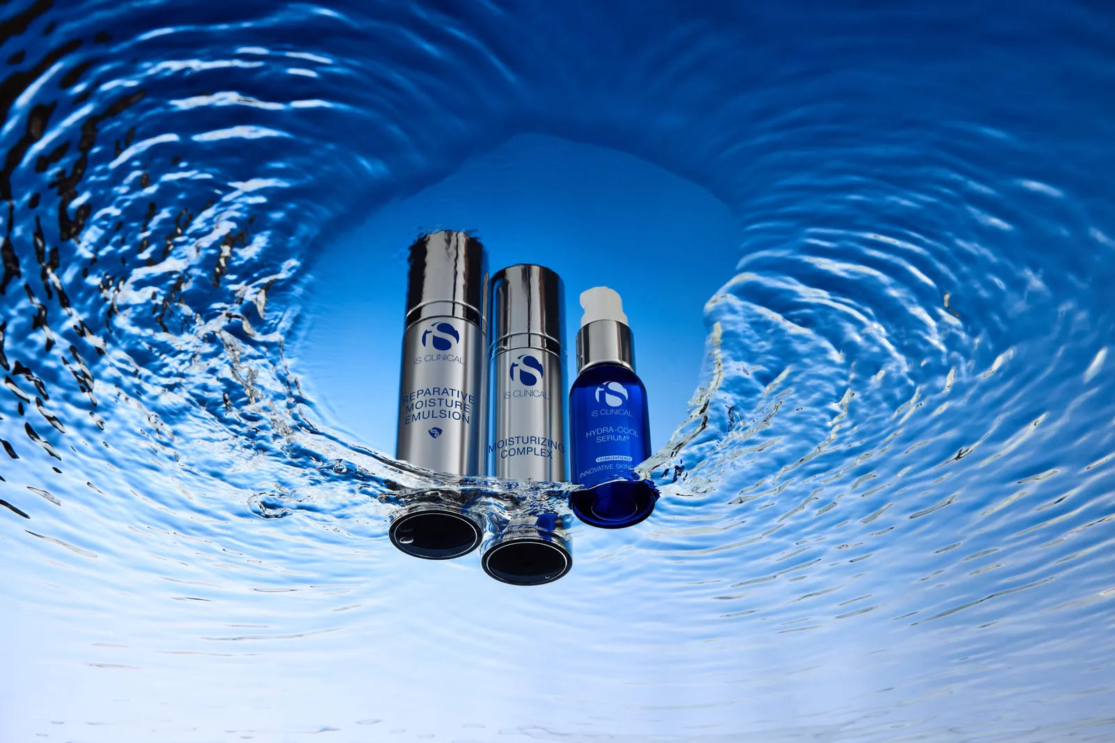 Three iS Clinical skincare bottles partially submerged in water with ripples on blue surface