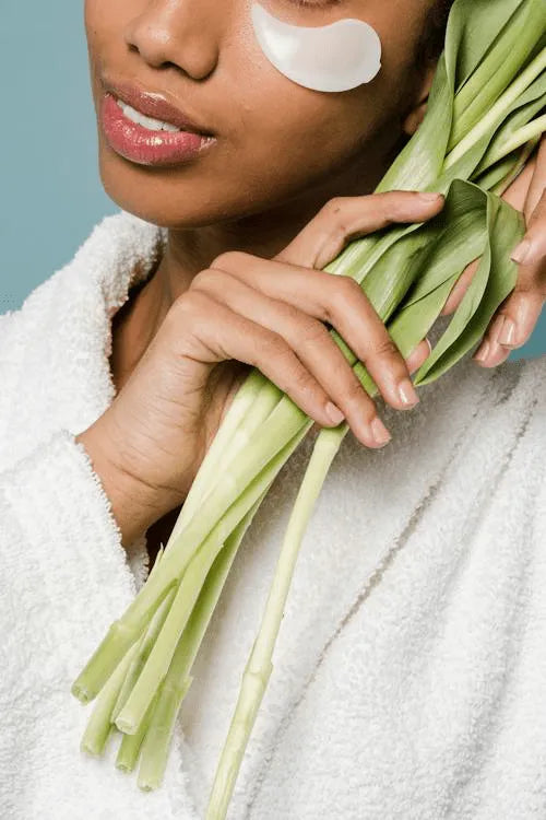 Close-up of a person wearing a white robe with a white under-eye patch, holding green leafy stems