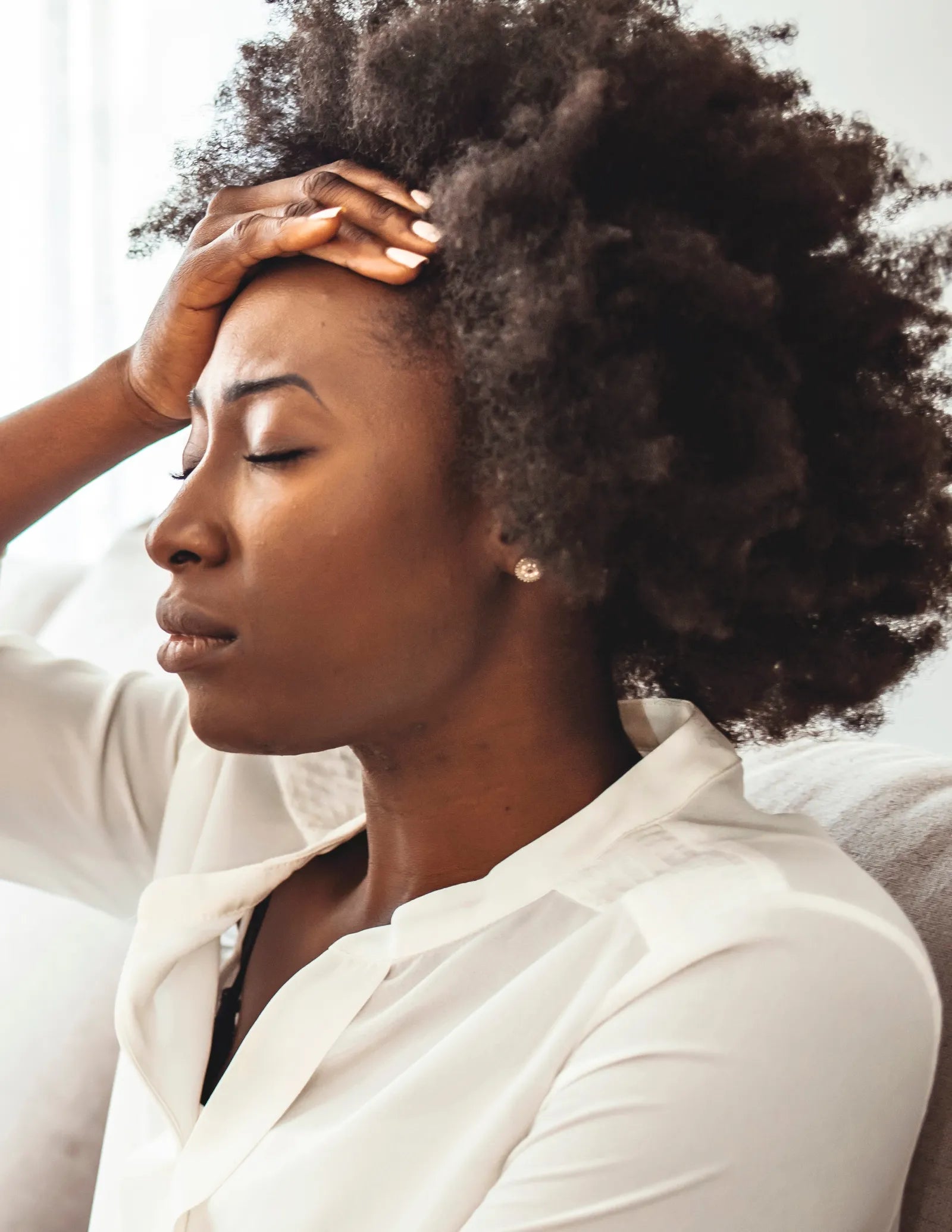 Woman with eyes closed holding forehead, appearing stressed or fatigued, wearing white shirt