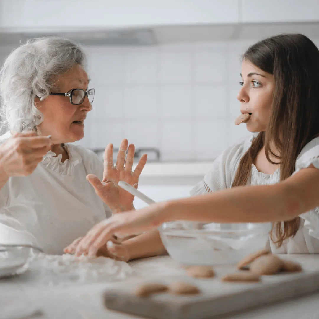 Older woman and teenage girl baking together in kitchen, girl tasting dough with finger