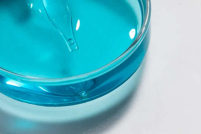 Close-up of bright blue serum with dropper inside a clear glass dish on white background