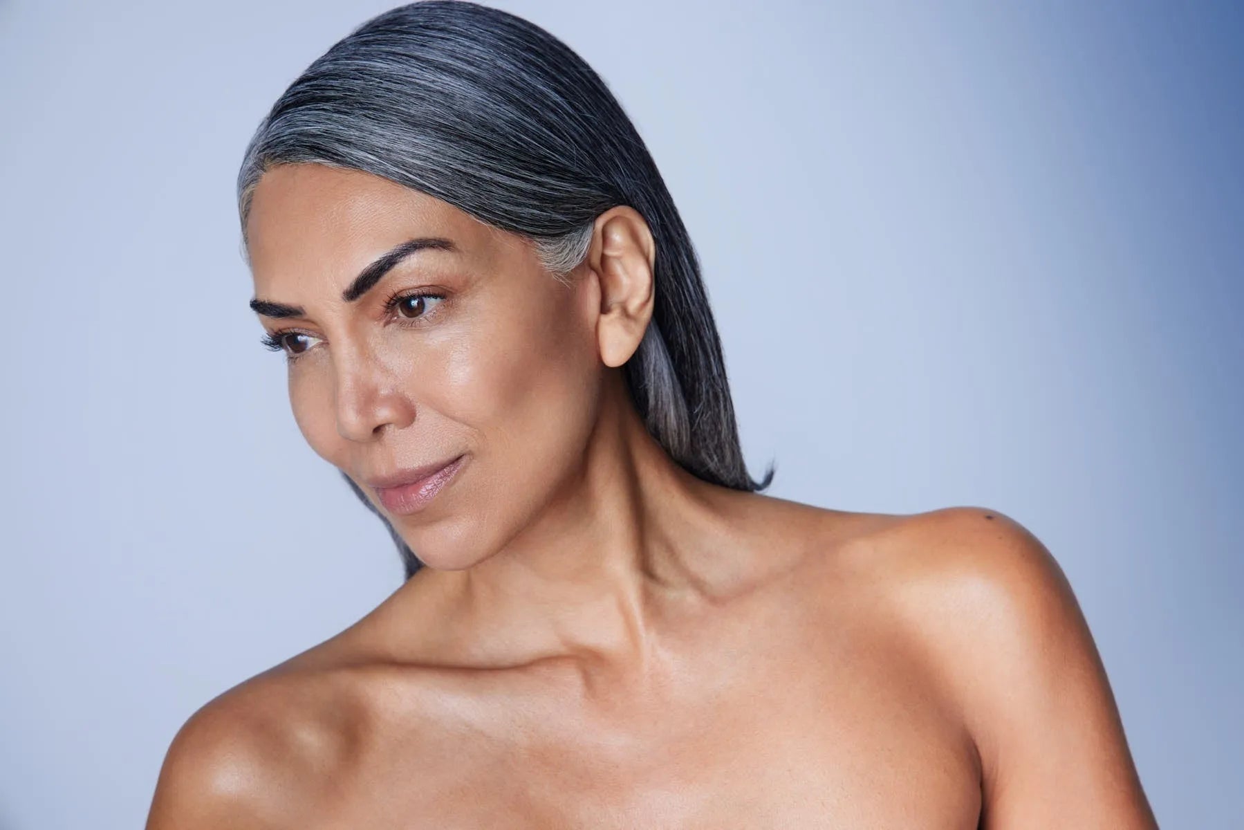 Mature woman with smooth skin and grey hair against a soft blue background