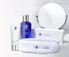 IS Clinical skincare products including a bottle, tube, and towel on a white surface with a mirror in the background.