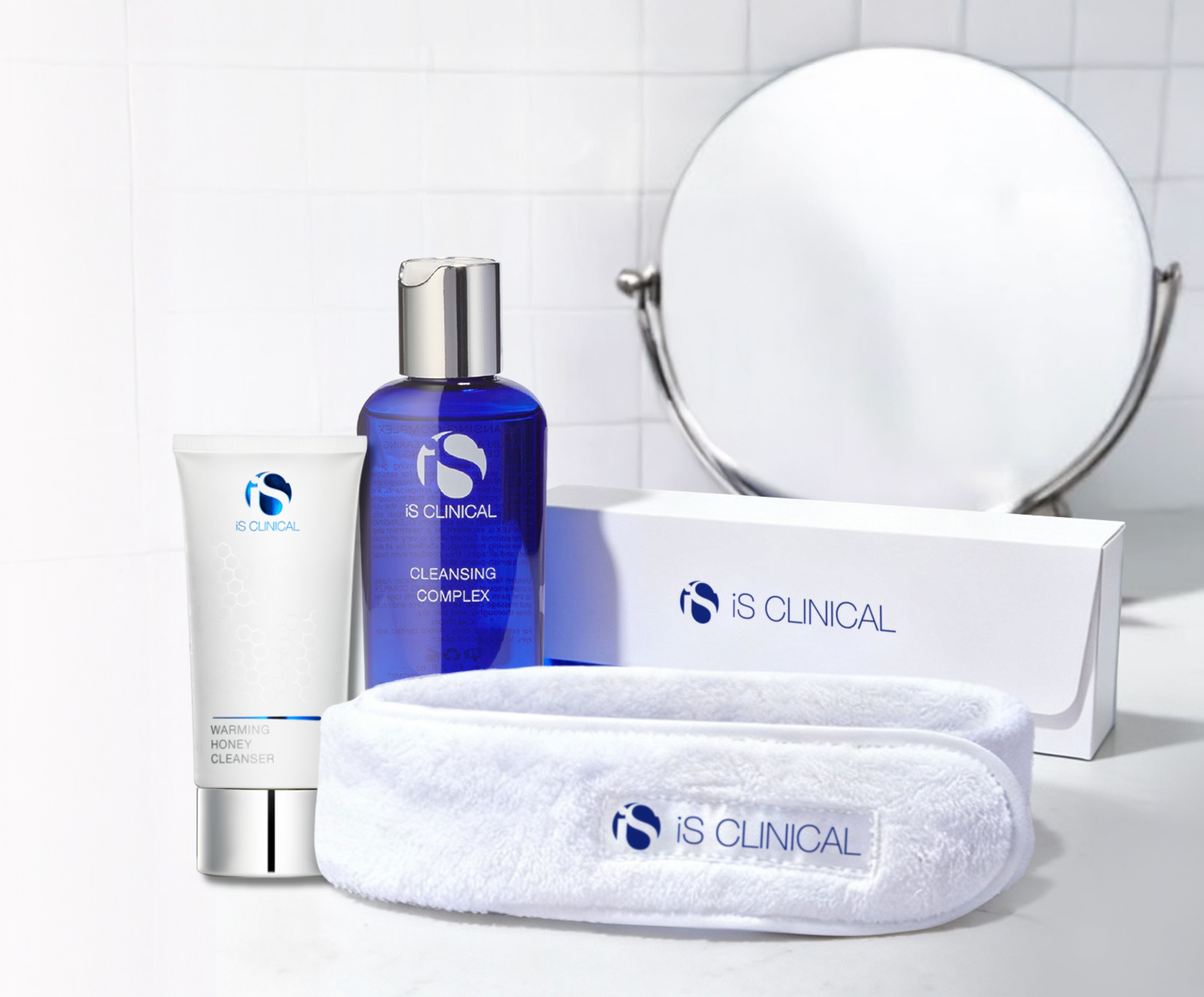 IS Clinical skincare products including a bottle, tube, and towel on a white surface with a mirror in the background.