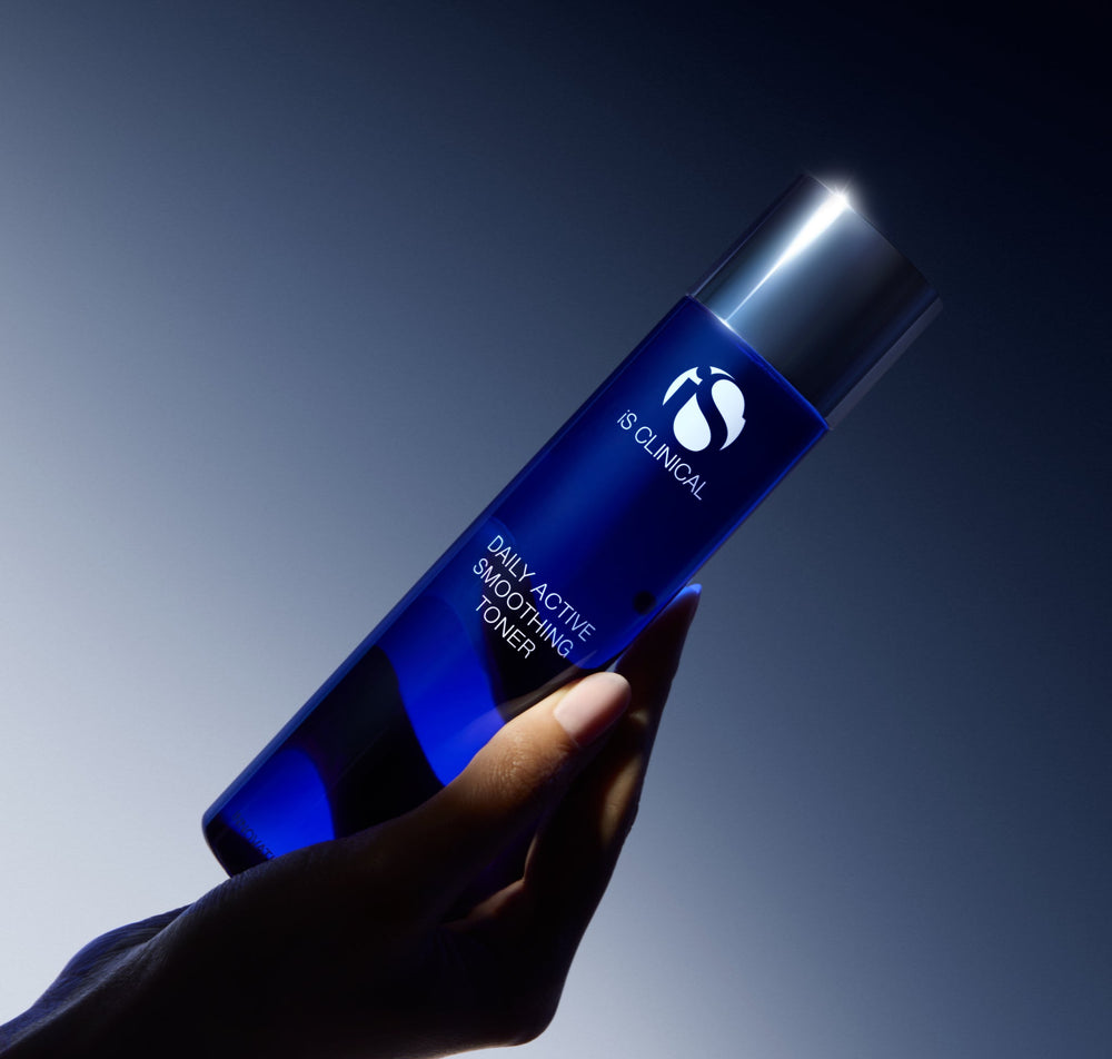 Hand holding the cobalt blue iS Clinical Daily Active Smoothing Toner bottle against a deep blue background