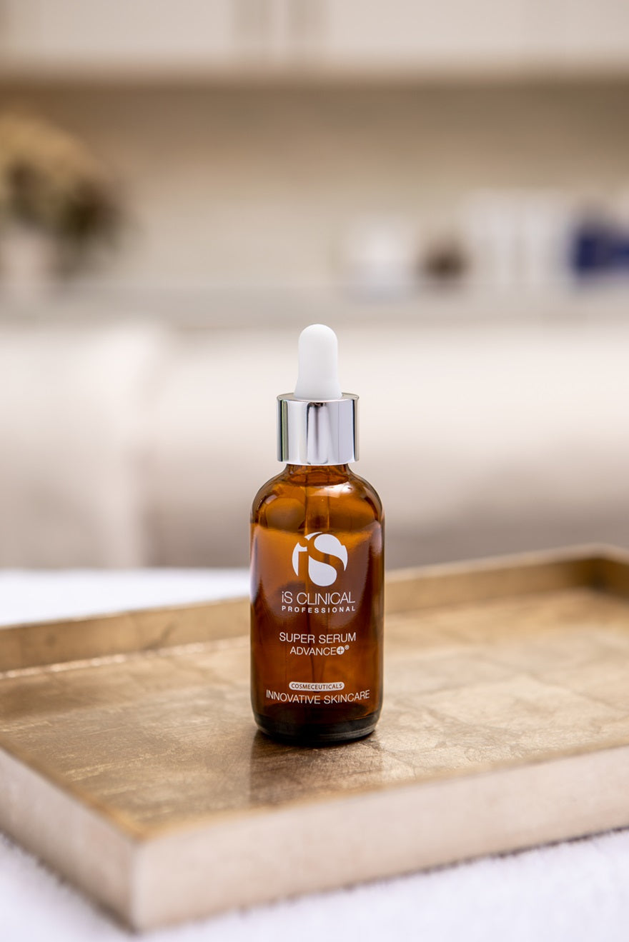 Amber glass bottle of iS Clinical Super Serum Advance+ with white dropper on gold tray