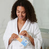 Woman in white robe holding iS Clinical Active Peel System packets numbered 1 and 2