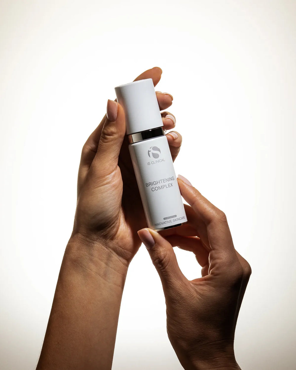 Hands holding a white pump bottle of iS Clinical Brightening Complex against a plain background