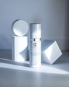 iS Clinical Brightening Complex bottle with silver cap against white geometric shapes on a white surface
