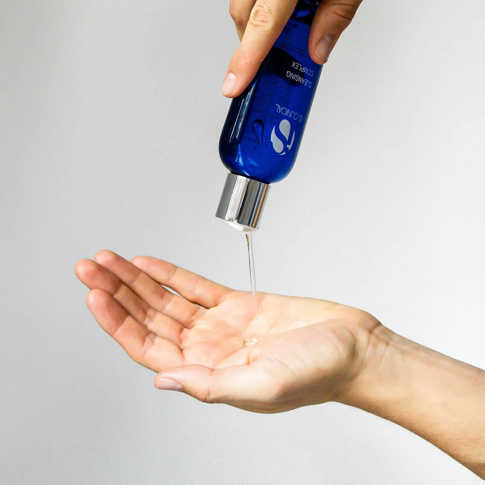 Hand dispensing clear gel from blue iS Clinical Cleansing Complex bottle onto palm