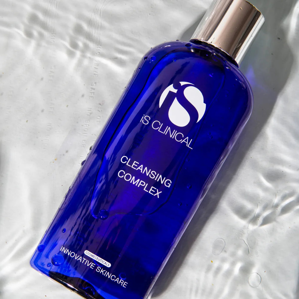 Blue bottle of iS Clinical Cleansing Complex with silver cap on rippled white surface