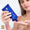Hand dispensing iS Clinical Cleansing Complex Polish from blue tube onto palm under water droplets