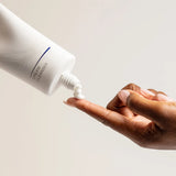 White tube of iS Clinical Cream Cleanser dispensing white cream onto a fingertip