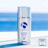 Silver bottle of iS Clinical Extreme Protect SPF 30 sunscreen with blue logo on white surface and ocean background