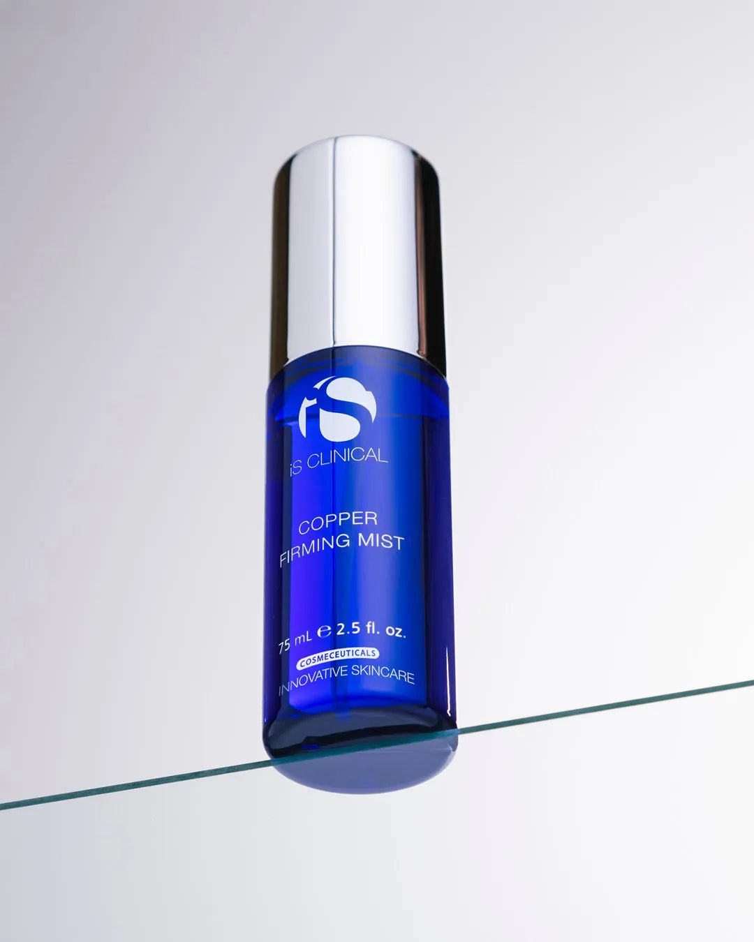 The iS Clinical Copper Firming Mist bottle resting on a glass surface