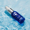 Blue iS Clinical Hydra-Cool Serum bottle with silver pump floating in clear water