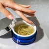 Hand scooping clear gel from open blue jar of iS Clinical Hydra-Intensive Cooling Mask on marble surface