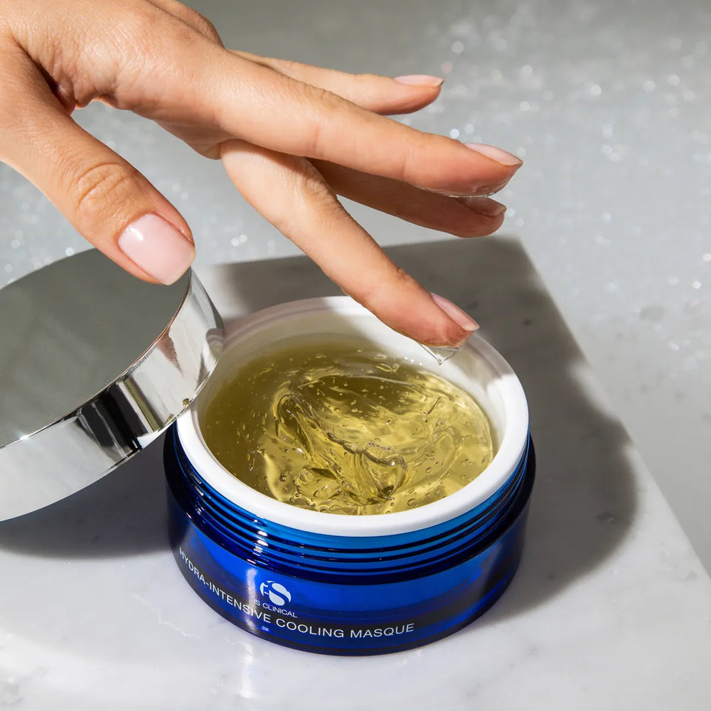Hand scooping clear gel from open blue jar of iS Clinical Hydra-Intensive Cooling Mask on marble surface