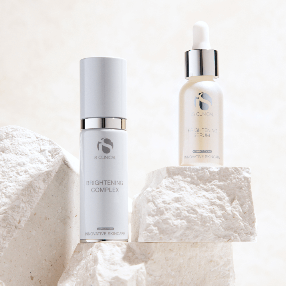 iS Clinical Brightening Complex pump bottle and Brightening Serum dropper bottle on textured white stone blocks