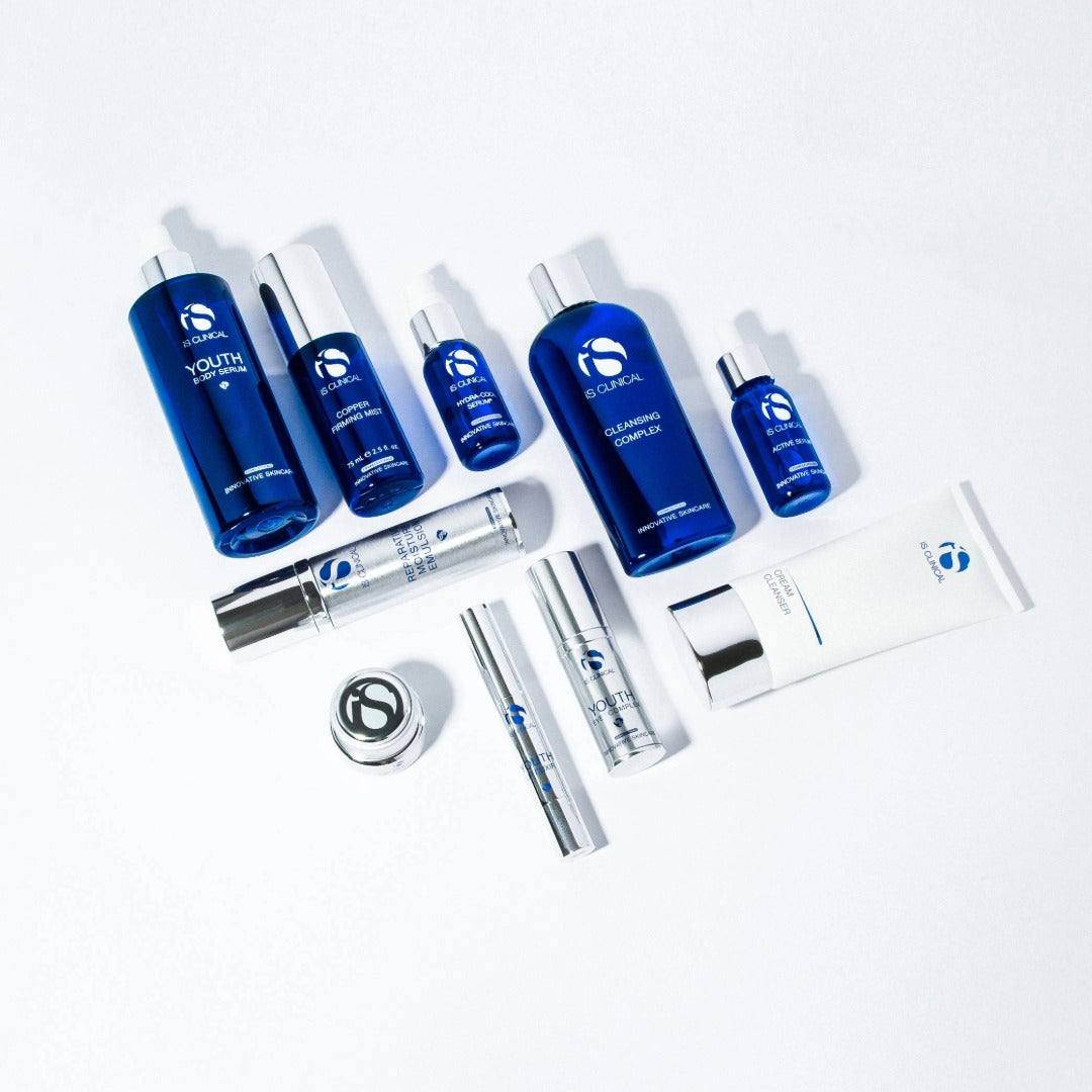 iS Clinical skincare products including blue bottles, silver tubes, and a white cream cleanser on white background