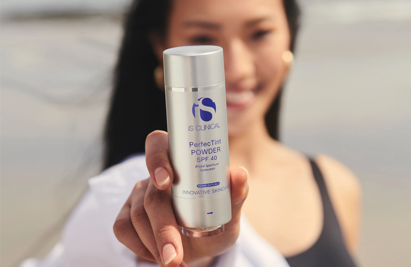 Hand holding iS Clinical PerfectTint Powder SPF 40 bottle with blurred person background