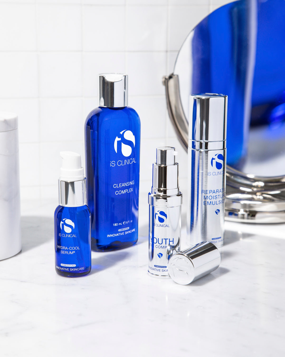 iS Clinical Cleansing Complex, Hydra-Cool Serum, Youth Eye Complex and Reparative Moisture Emulsion on a marble bathroom shelf