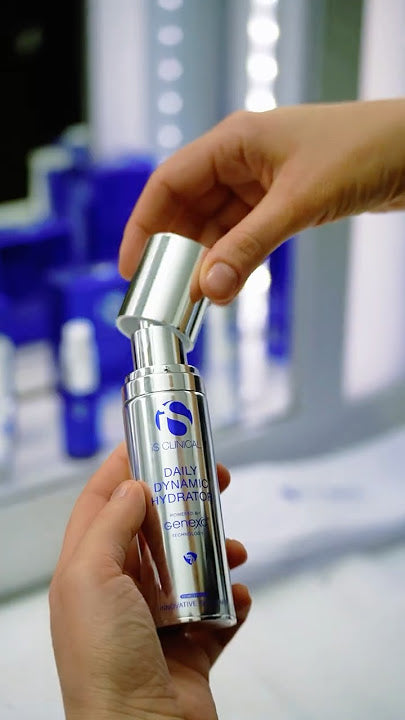Hands holding iS Clinical Daily Dynamic Hydrator bottle with silver pump and blue label text