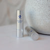 Two silver tubes of iS Clinical LiProtect SPF 35 lip balm on white surface with textured stone background