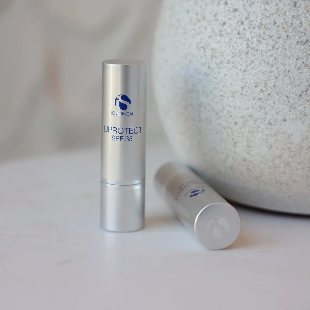 Two silver tubes of iS Clinical LiProtect SPF 35 lip balm on white surface with textured stone background