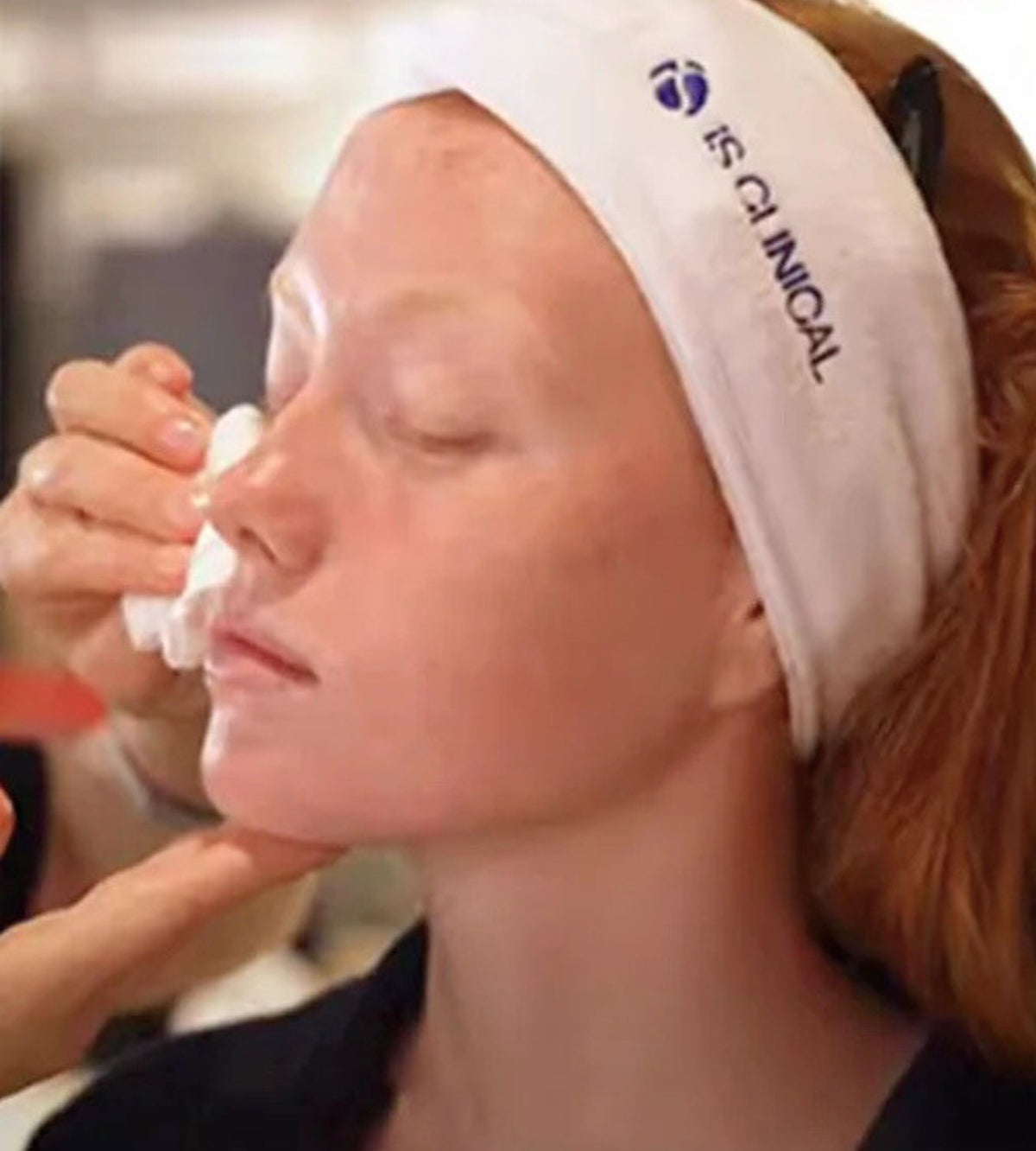 Person wearing white iS Clinical headband having skin gently wiped with cotton pad