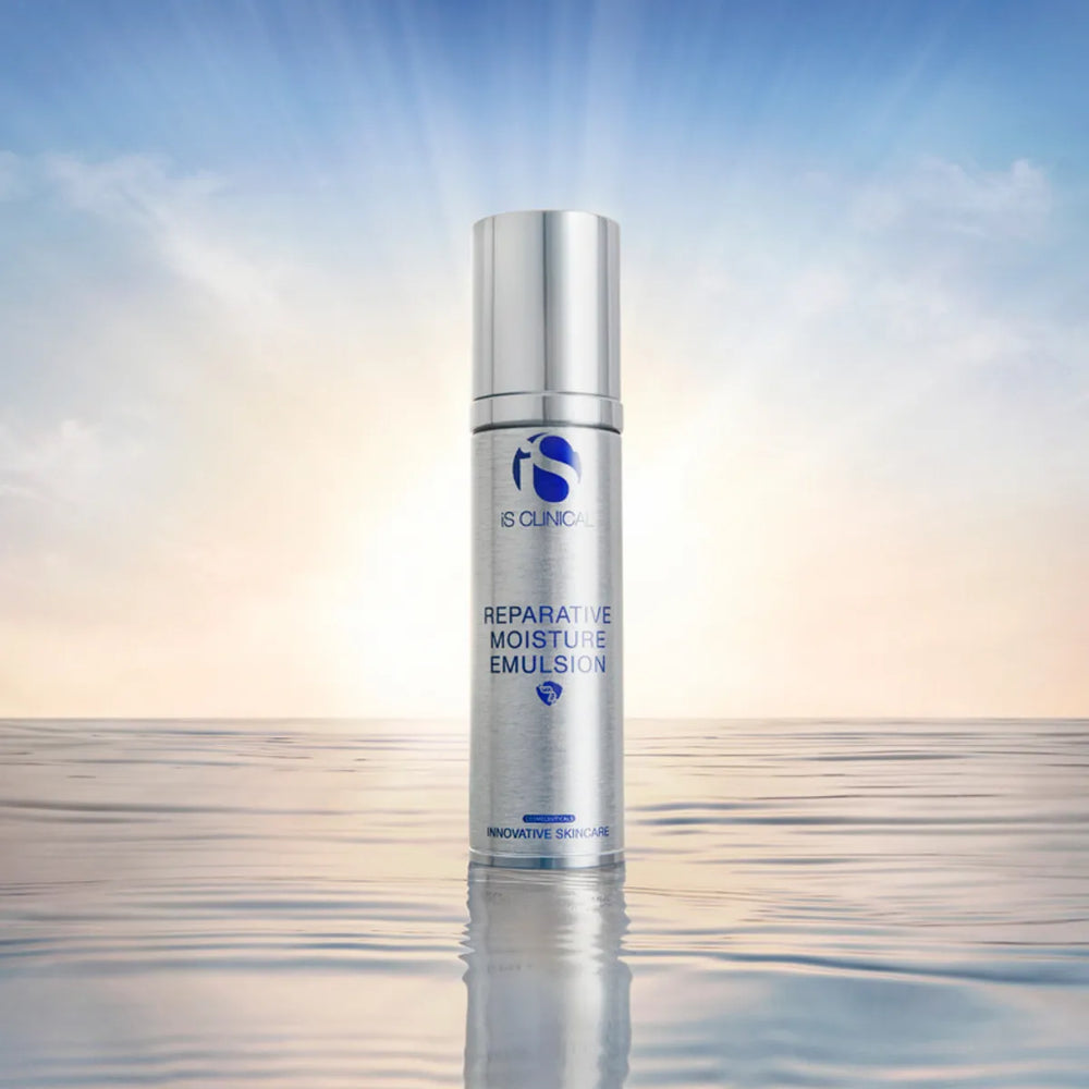 Silver bottle of iS Clinical Reparative Moisture Emulsion 50g standing on reflective water surface with sunrise background