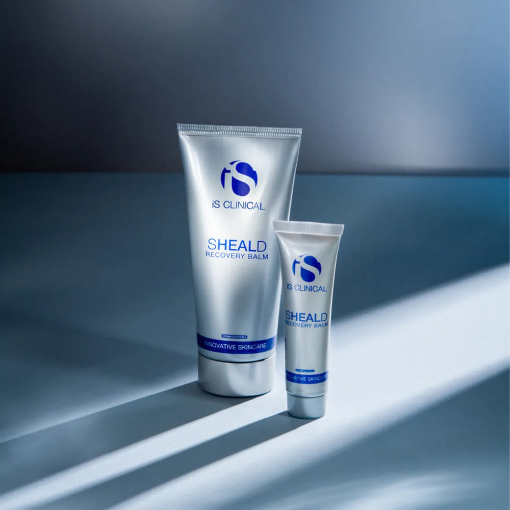 Two silver tubes of iS Clinical SHEALD Recovery Balm with blue branding on a blue surface
