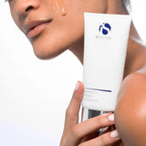 Person holding iS Clinical Warming Honey Cleanser tube with honey-coloured cleanser on cheek
