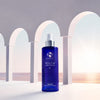 Blue pump bottle of iS Clinical Youth Body Serum with white arches and ocean background
