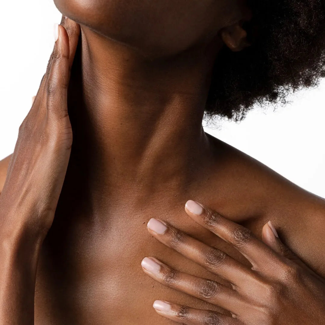 Close-up of a person gently touching their neck and shoulder skin against a white background
