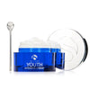 Open blue jar of iS Clinical Youth Intensive Crème with white cream and silver spatula on white background